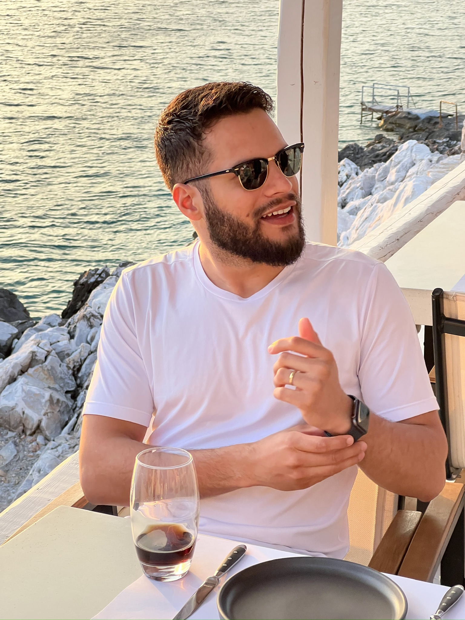 Carlos smiling warmly at the camera in a well-lit indoor setting with a neutral background, conveying a friendly and approachable mood
